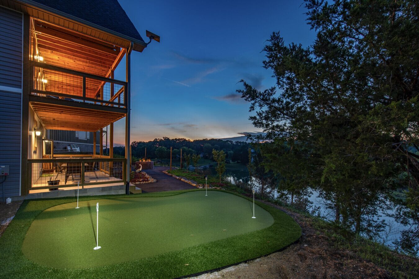 Una casa con porche cubierto y campo de práctica de golf junto a un lago.
