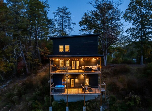 A two-story cabin with a hot tub on the ground floor, surrounded by trees.
