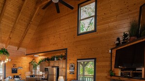A cozy cabin interior with a wooden ceiling, a fireplace, a sectional sofa, and a dining area. - The Real McCoy | Epic Views, Hot Tub, Arcade! (Sevierville)