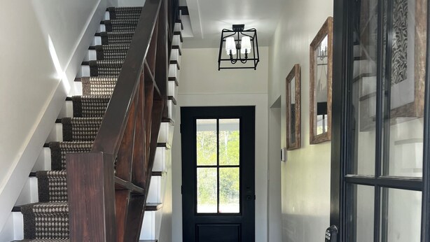 Eine Treppe mit dunklen Holzstufen und einem Geländer, die zu einer Tür mit Glasfenster und schwarzem Rahmen führt.