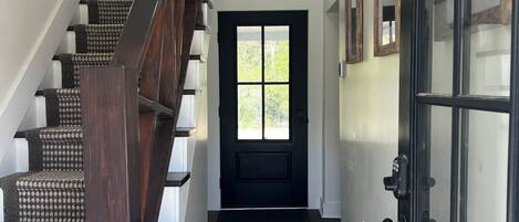 A staircase with dark wood steps and a handrail, leading to a door with a glass panel and a black frame.