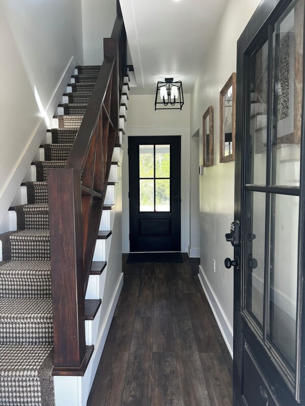 Una escalera con escalones de madera oscura y una barandilla, que conduce a una puerta con un panel de vidrio y un marco negro.