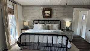 Ein Schlafzimmer mit einem Bett, zwei Nachttischen, einem Wandbild und einem Fenster mit Vorhängen.