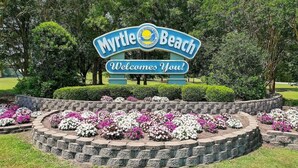 A sign welcoming visitors to Myrtle Beach with a circular flower bed in the foreground. - 1BR New Oceanfront with Heated Pools, Coral Beach! (Myrtle Beach)