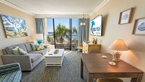 A hotel room with a sofa, a dining table, a TV, and a view of the ocean. - 1BR New Oceanfront with Heated Pools, Coral Beach! (Myrtle Beach)