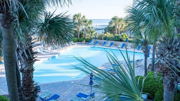 A pool area with blue lounge chairs and palm trees. - 1BR New Oceanfront with Heated Pools, Coral Beach! (Myrtle Beach)
