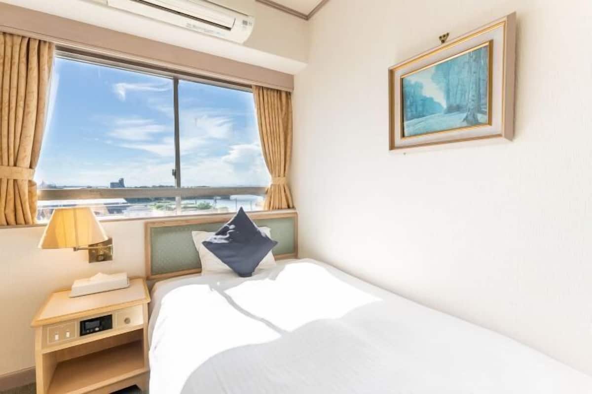 Habitación de hotel con cama, mesita de noche con lámpara, un cuadro en la pared y una ventana con cortinas.