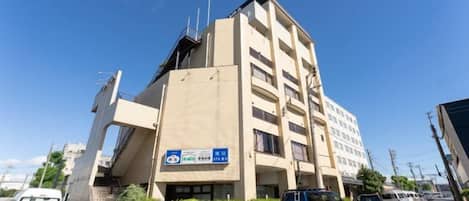 A multi-story building with a flat facade, a blue sign with white text, and a parking area with cars.