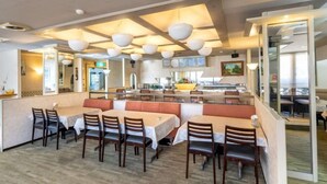 Un restaurant doté de nombreuses tables et de plusieurs coins repas, d’une cuisine et offrant une vue sur la mer.