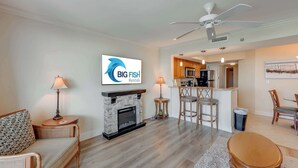 A living room with a fireplace, a sofa, a dining table, and a kitchen area in the background. - New 2BR at Horizon at 77th with Views,Nice Pools! (Myrtle Beach)