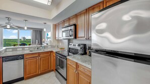 A modern kitchen with wooden cabinets, stainless steel appliances, and a view of a green landscape. - New 2BR at Horizon at 77th with Views,Nice Pools! (Myrtle Beach)