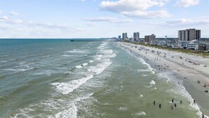 Une plage avec des vagues, un rivage sablonneux et des bâtiments en arrière-plan.
