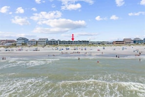 A beach with multiple buildings in the background, a clear sky, and waves in the foreground.