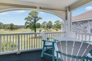 A covered outdoor area with a view of a golf course, a table, and two chairs. - NEW, Large 2 BR at Magnolia Place,Golf Course View (Myrtle Beach)