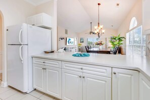 A kitchen with white cabinets, a refrigerator, a dining area with a table and chairs, and a chandelier. - NEW, Large 2 BR at Magnolia Place,Golf Course View (Myrtle Beach)