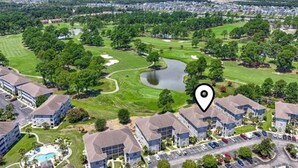 Um campo de golfe com um lago, rodeado por edifícios residenciais e parques de estacionamento.