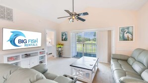 Sala de estar com sofá, mesa de centro, ventilador de teto e uma TV exibindo 'BIG FISH RENTALS'.