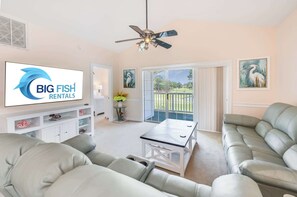 A living room with a sofa, a coffee table, a ceiling fan, and a TV displaying 'BIG FISH RENTALS'. - NEW, Large 2 BR at Magnolia Place,Golf Course View (Myrtle Beach)