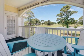 A porch with a table and chairs, a door with shutters, and a view of a golf course. - NEW, Large 2 BR at Magnolia Place,Golf Course View (Myrtle Beach)