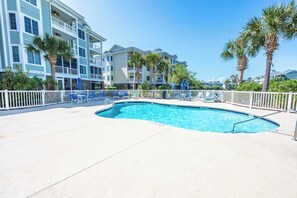 Une piscine avec des chaises longues, des palmiers et un immeuble à plusieurs étages doté de balcons.