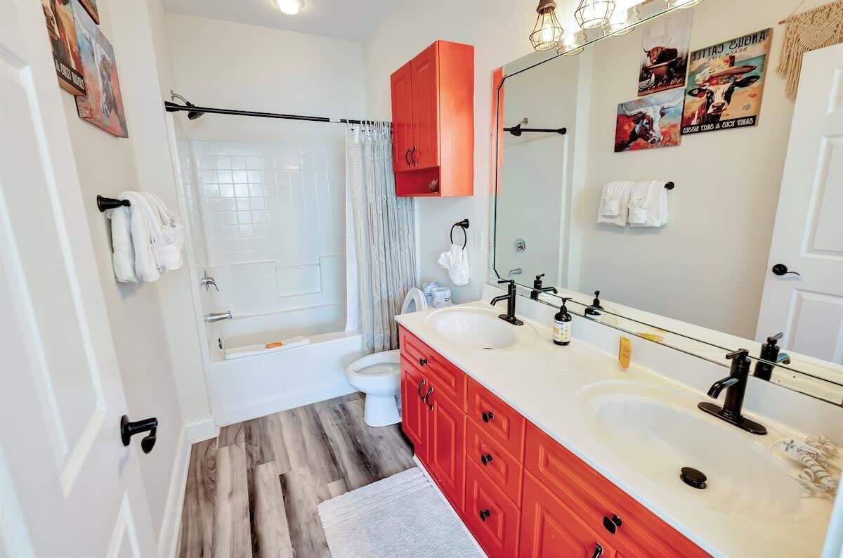 Een badkamer met douche, toilet en een wastafelmeubel met rode kastjes.