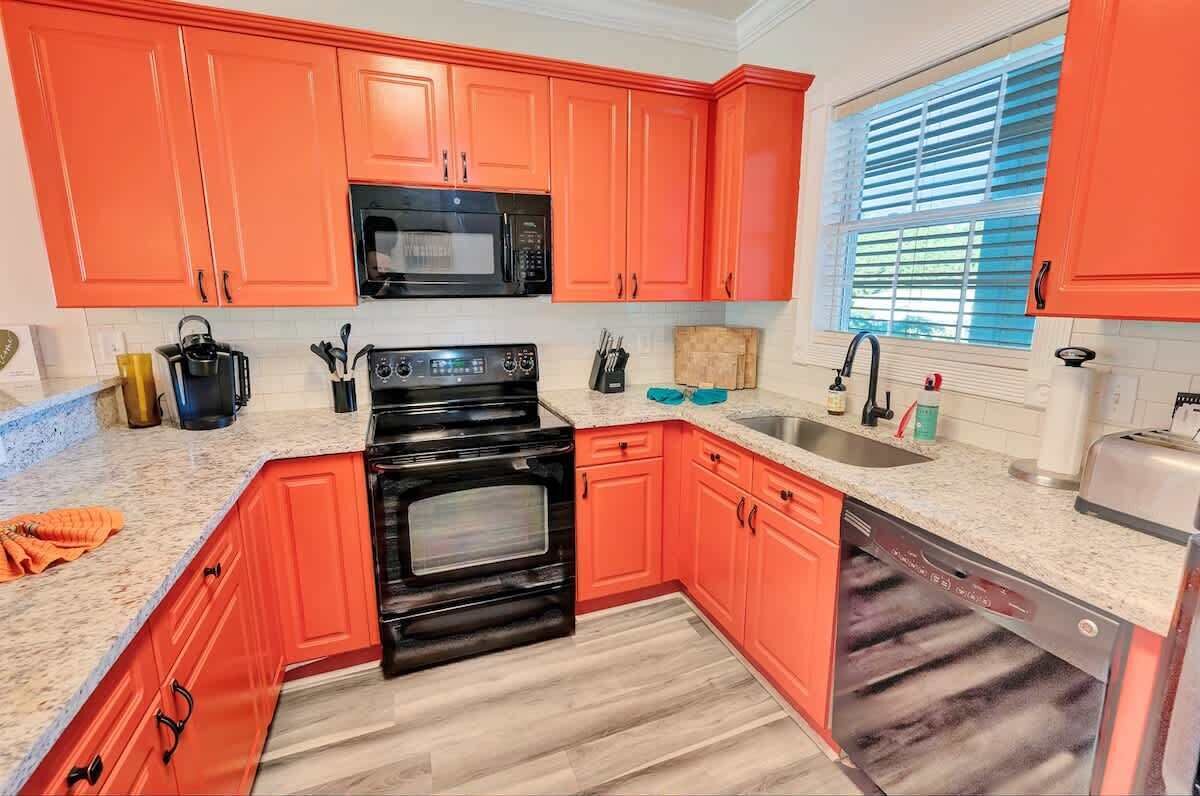 A kitchen with red cabinets, a black microwave, a stove, and a dishwasher.
