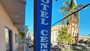 Un panneau bleu indiquant « HÔTEL CENTRAL », offrant une vue dégagée sur la façade de l’immeuble, notamment sur le trottoir et les voitures garées.
