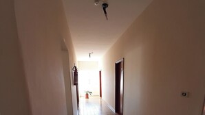 Un couloir avec un sol carrelé, un ventilateur de plafond et une porte sur le côté droit.