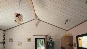 A cozy cabin interior with a wooden ceiling, a sofa, a kitchen area, and a view through a door. - "MOUTY": A DELIGHTFUL WOODEN CHALET AT THE EDGE OF THE FOREST (Le Chambon-sur-Lignon)
