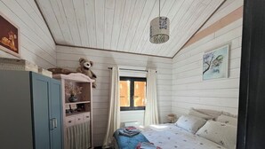 A bedroom with a bed, a wardrobe, a window with curtains, a hanging light fixture, and a teddy bear on the wardrobe. - "MOUTY": A DELIGHTFUL WOODEN CHALET AT THE EDGE OF THE FOREST (Le Chambon-sur-Lignon)
