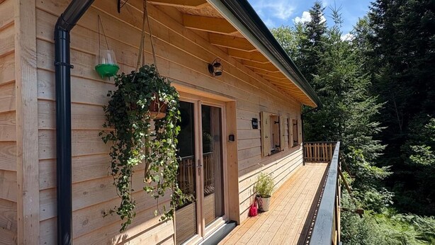 A wooden cabin with a deck, a hanging planter, and a view of a forest. - "MOUTY": A DELIGHTFUL WOODEN CHALET AT THE EDGE OF THE FOREST (Le Chambon-sur-Lignon)