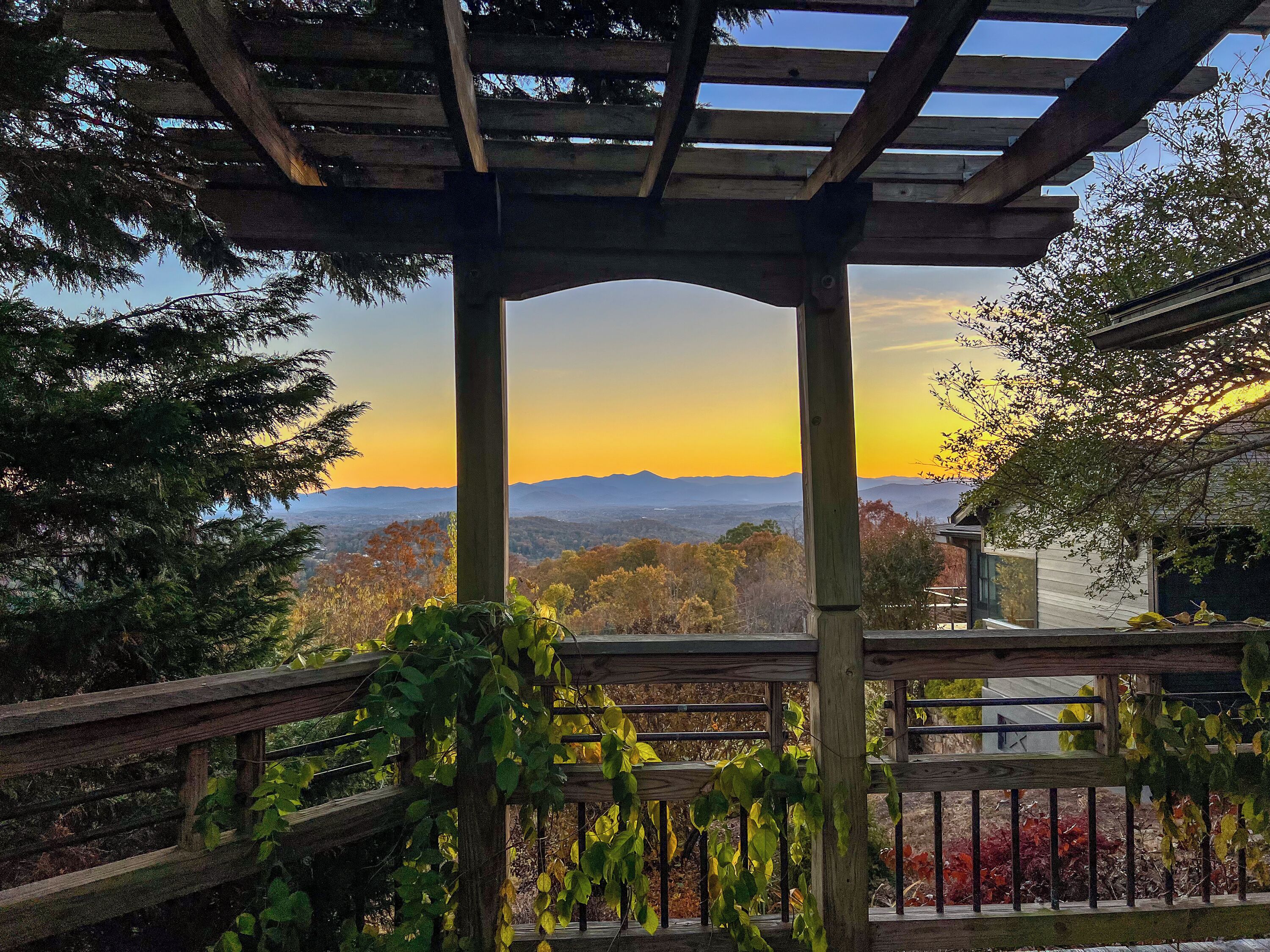 Une pergola en bois offrant une vue sur un coucher de soleil sur les montagnes.
