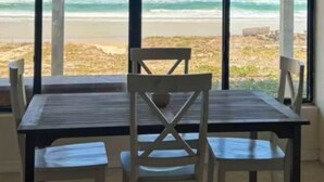 Una habitación con un ventanal grande que da a la playa. Hay una mesa con cuatro sillas.