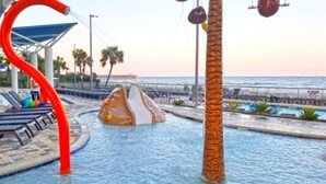 Un espace piscine avec un toboggan aquatique, un palmier et une vue sur l’océan.