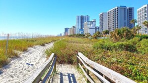A beach path leading to a cityscape with high-rise buildings. - Direct 1BR Oceanfront Views at Palms - Nice Pools (Myrtle Beach)