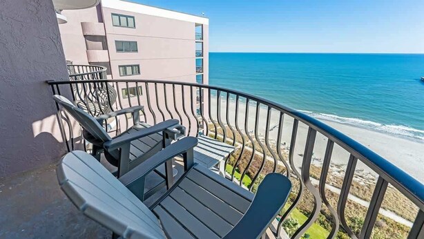 A balcony with outdoor furniture overlooking a beach and a building. - Direct 1BR Oceanfront Views at Palms - Nice Pools (Myrtle Beach)