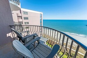 A balcony with outdoor furniture overlooking a beach and a building. - Direct 1BR Oceanfront Views at Palms - Nice Pools (Myrtle Beach)