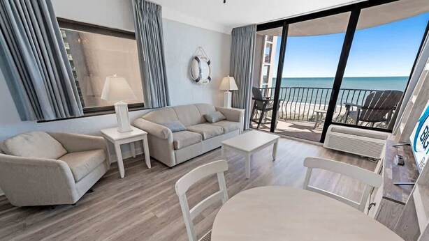Ett modernt hotellrum med en balkong, en soffa, ett soffbord och ett matbord.