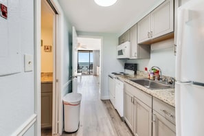 A narrow kitchen with white cabinets, a microwave, a sink, and a trash bin.
