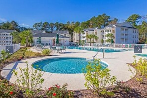 A pool area with a circular pool, lounge chairs, and a building with balconies. - NEW Large 2BR- Pools - River Oaks Golf - Hot Tubs (Myrtle Beach)