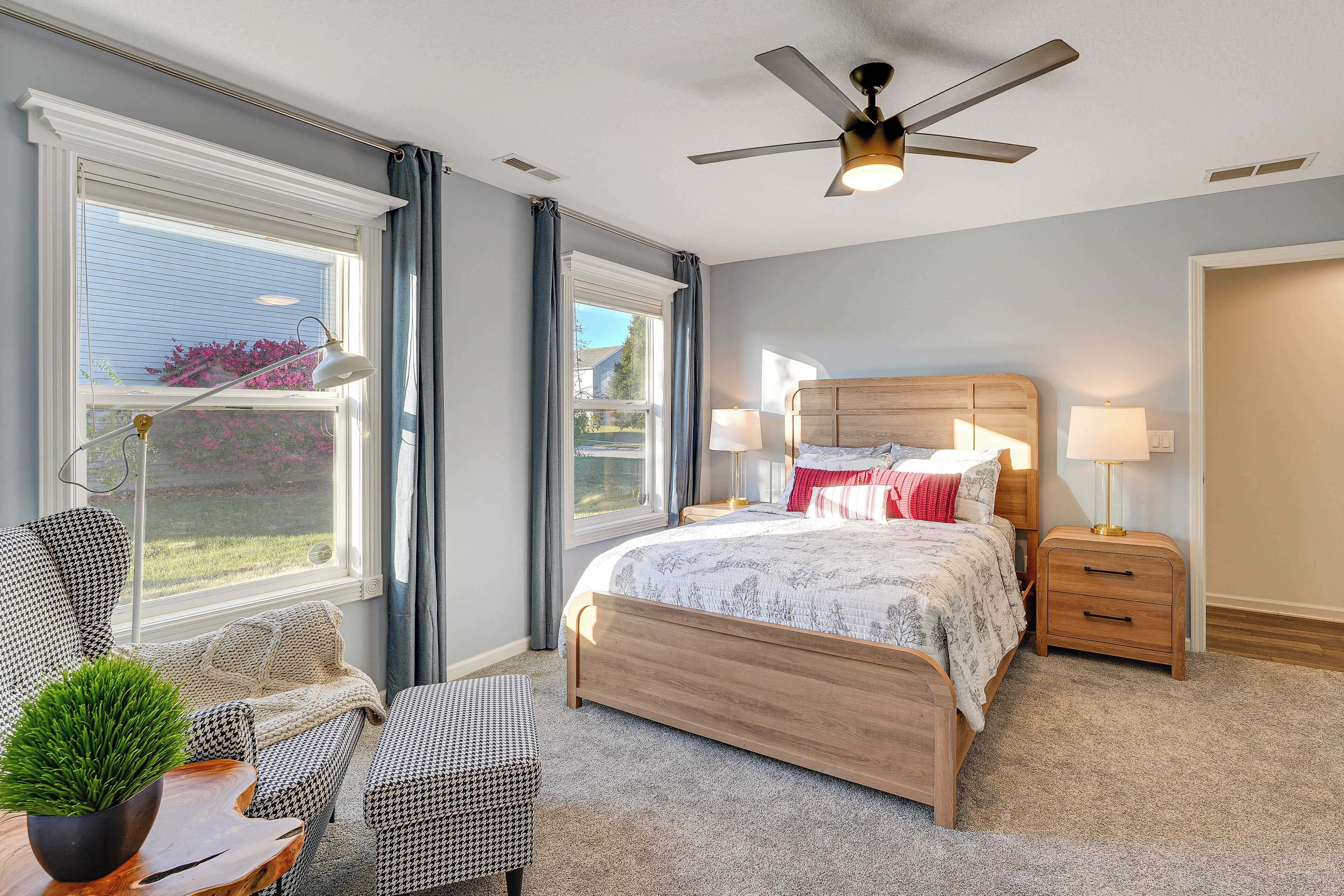 Un dormitorio con cama, mesitas de noche, ventilador de techo y ventana con cortinas.