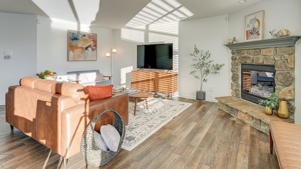 A modern living room with a stone fireplace, a leather sofa, a flat-screen TV, and a large window allowing natural light. - Private Yard + Pond Views: Fort Wayne Family Home! (Fort Wayne)
