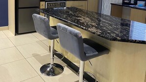 Una cocina moderna con encimera de granito, electrodomésticos de acero inoxidable y dos taburetes de bar.