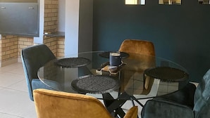 Un comedor con una mesa de vidrio rodeada de sillas de terciopelo, una chimenea de ladrillo y una pared oscura con ventanas arqueadas.