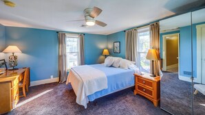 A bedroom with a bed, bedside tables, a ceiling fan, and a large window with curtains.