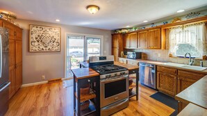 A modern kitchen with wooden cabinets, stainless steel appliances, and a large window with decorative curtains.
