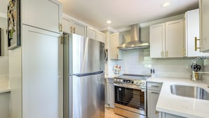 A modern kitchen with stainless steel appliances, white cabinetry, and a central island. - Global Staycation! Scenic Pikesville Family Home (Pikesville)