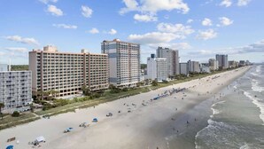 A beachfront hotel with multiple high-rise buildings, a sandy beach, and a clear sky. - Studio Sand Castle South,Direct Ocean View, Pools! (Myrtle Beach)