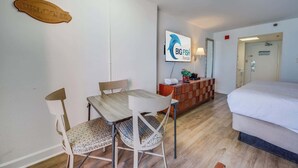 A hotel room with a bed, a wooden dining table with chairs, a TV mounted on the wall, and a small cabinet. - Studio Sand Castle South,Direct Ocean View, Pools! (Myrtle Beach)