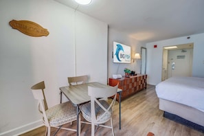 A hotel room with a bed, a wooden dining table with chairs, a TV mounted on the wall, and a small cabinet.